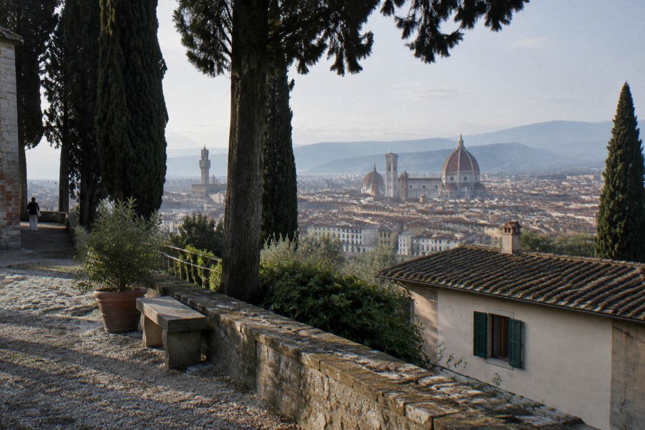 From a cypress-shaded hillside terrace above the abbey, terracotta rooftops spreading toward the cathedral's great dome, dew on the gravel, one window shutter half open below