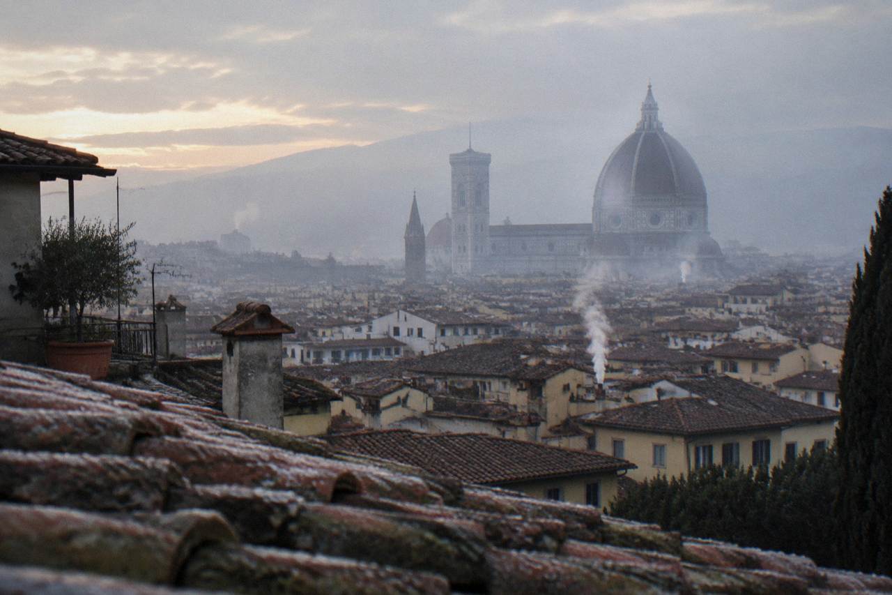 High over jumbled terracotta rooftops as Brunelleschi's great tiled dome rises through the haze, chimney smoke drifting, dew on the nearest ridge tiles
