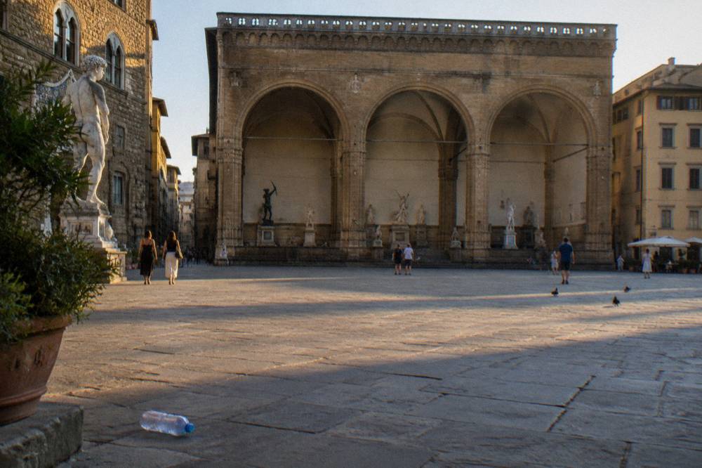 The open stone arches of the Loggia dei Lanzi seen from the far side of Piazza della Signoria, the arches in warm light with only small dark shapes inside them
