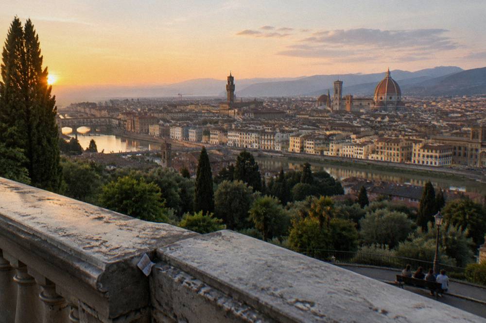 From the corner of the hilltop stone balustrade looking down over the Arno, the dome and Giotto's bell tower catching last golden light, a crumpled ticket stub wedged in the parapet joint
