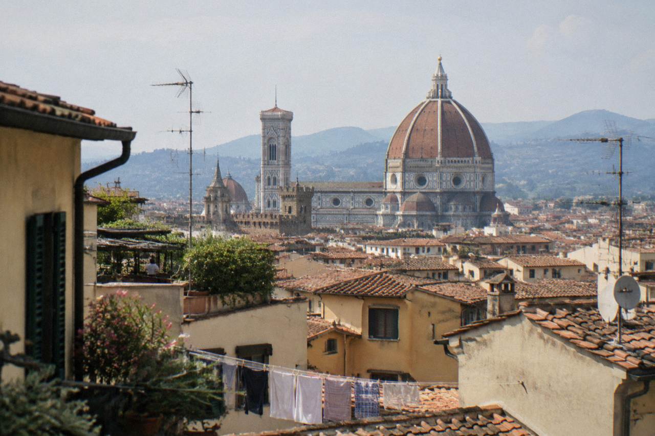 Seen high across a jumble of ochre plaster and terracotta rooftops, the cathedral's great brick dome and white marble drum dominating the skyline, Rooftops of the historic centre near the Duomo