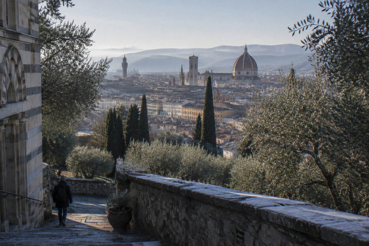 From the shaded staircase terrace beside the abbey church, olive trees framing a spread of terracotta rooftops with the great tiled dome above, frost still riming the low stone parapet
