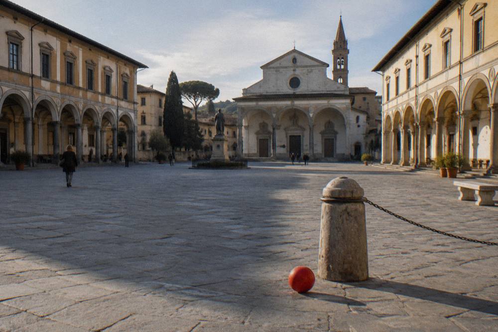 Across the open stone square toward the symmetrical ochre arcaded palace facades, a child's abandoned red ball near a scuffed bollard, long shadows raking the paving