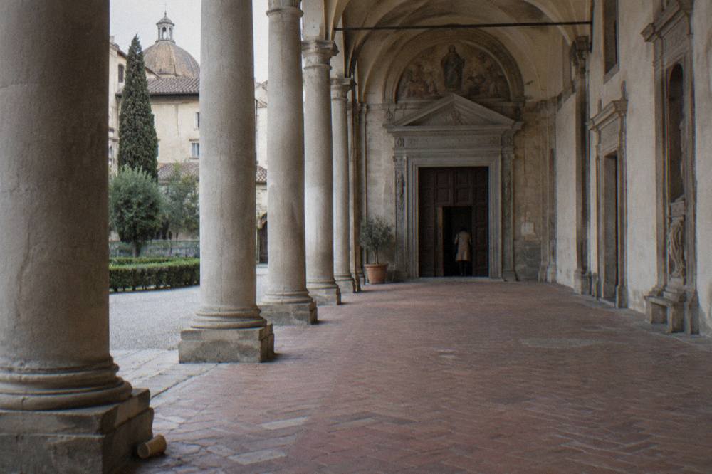 Under the broad arched portico of the Santissima Annunziata church, pale stone columns and worn terracotta paving receding along the arcade