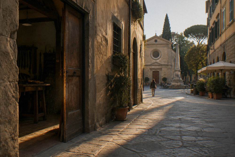 Old workshop facades of pietra forte and faded ochre render, a scuffed wooden doorway left half open, dust drifting in the slanting sun, Piazza Santo Spirito