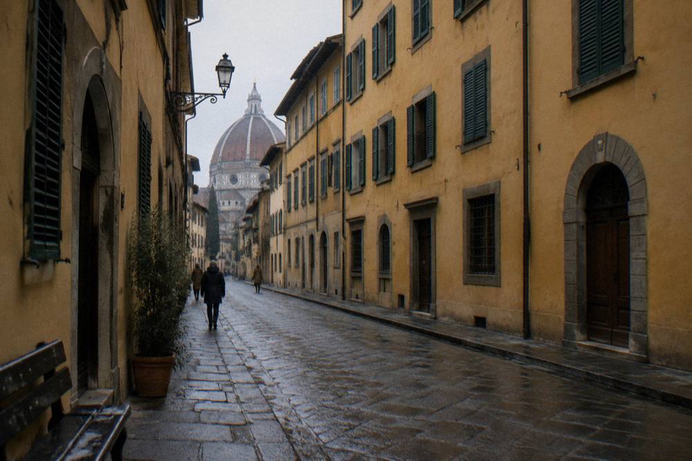 Looking along Via Cavour between tall ochre plaster palazzi, wet cobbles, closed green shutters, two distant pedestrians from behind, one scuffed bench edge in shadow