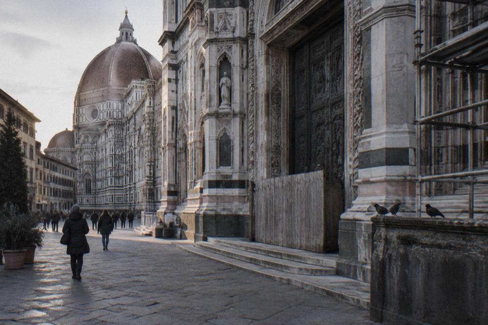 Cold winter afternoon in the piazza of Florence Cathedral in Italy, the striped white and green marble facade lit low from the west, scaffolding poles on one flank