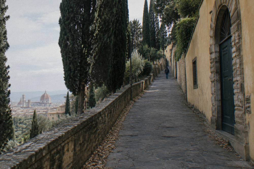 Seen up a steep cypress-lined lane climbing from the San Niccolo district between ochre plastered walls and rusticated stone doorways, fallen leaves gathered in the gutter