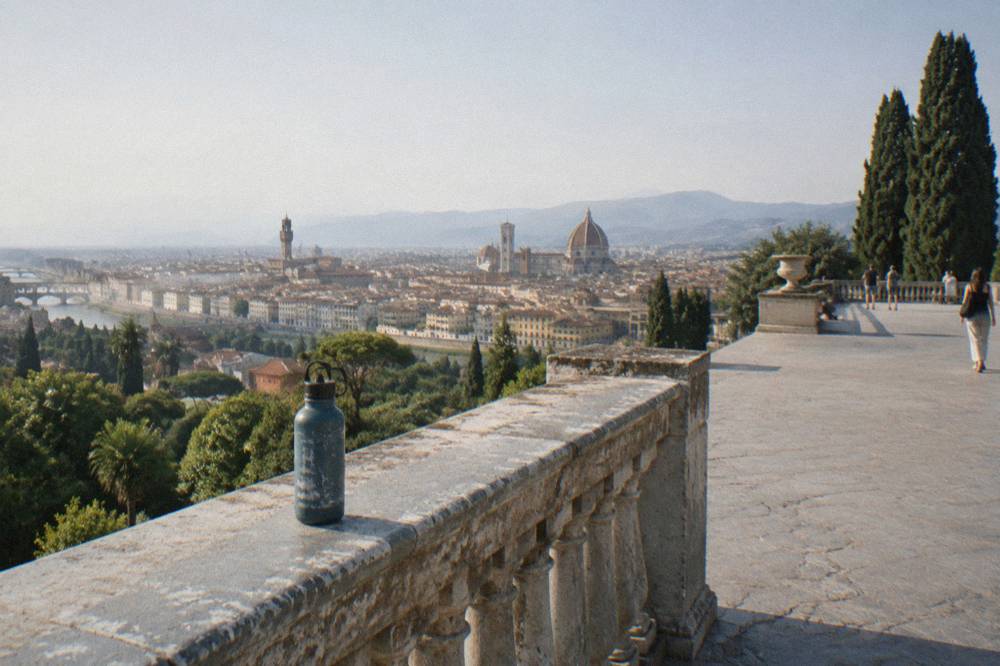 Low along the worn stone balustrade of the Piazzale Michelangelo terrace, sun-bleached paving stretching across the open esplanade, a scuffed water bottle left on the parapet