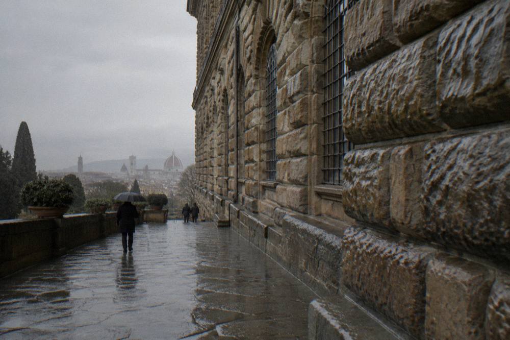 Low close view along the rusticated stone blocks of Palazzo Pitti's facade, wet masonry darkening, arched windows receding, rain beading on the deep-jointed pietra forte