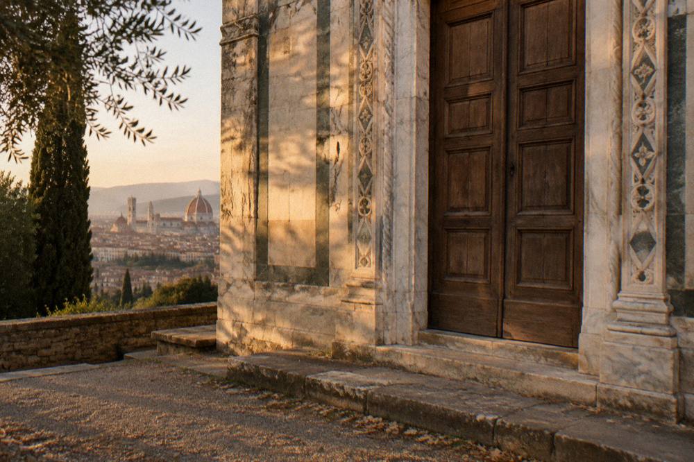 The tall closed wooden doors of San Miniato al Monte set in their carved marble doorway, golden light raking across weathered stone, a scuffed step and scattered leaf litter below