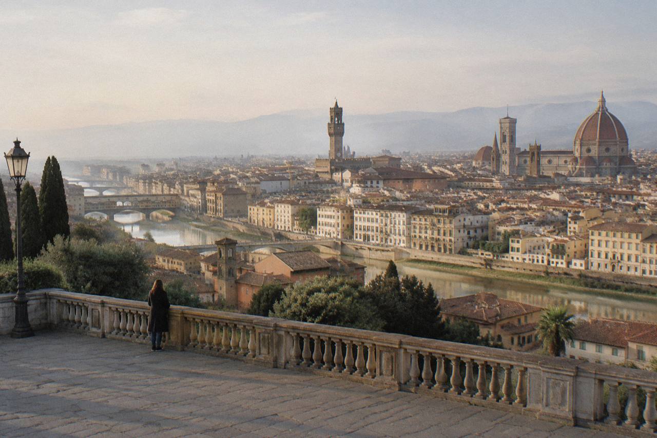Late afternoon view from the stone terrace of Piazzale Michelangelo looking down on Florence, the great dome of the cathedral and Giotto's Bell Tower rising above a sea of terracotta rooftops, the Arno curving through the city with Ponte Vecchio spanning it, soft golden light on the river and hills beyond.